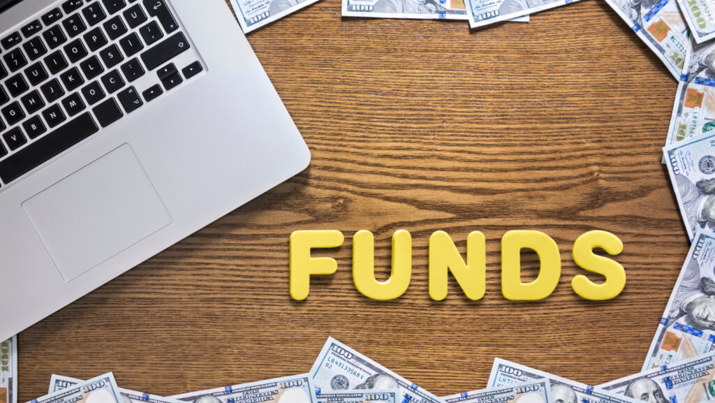 desk with laptop and $100 dollar bills around it with the words "funds" written in yellow.